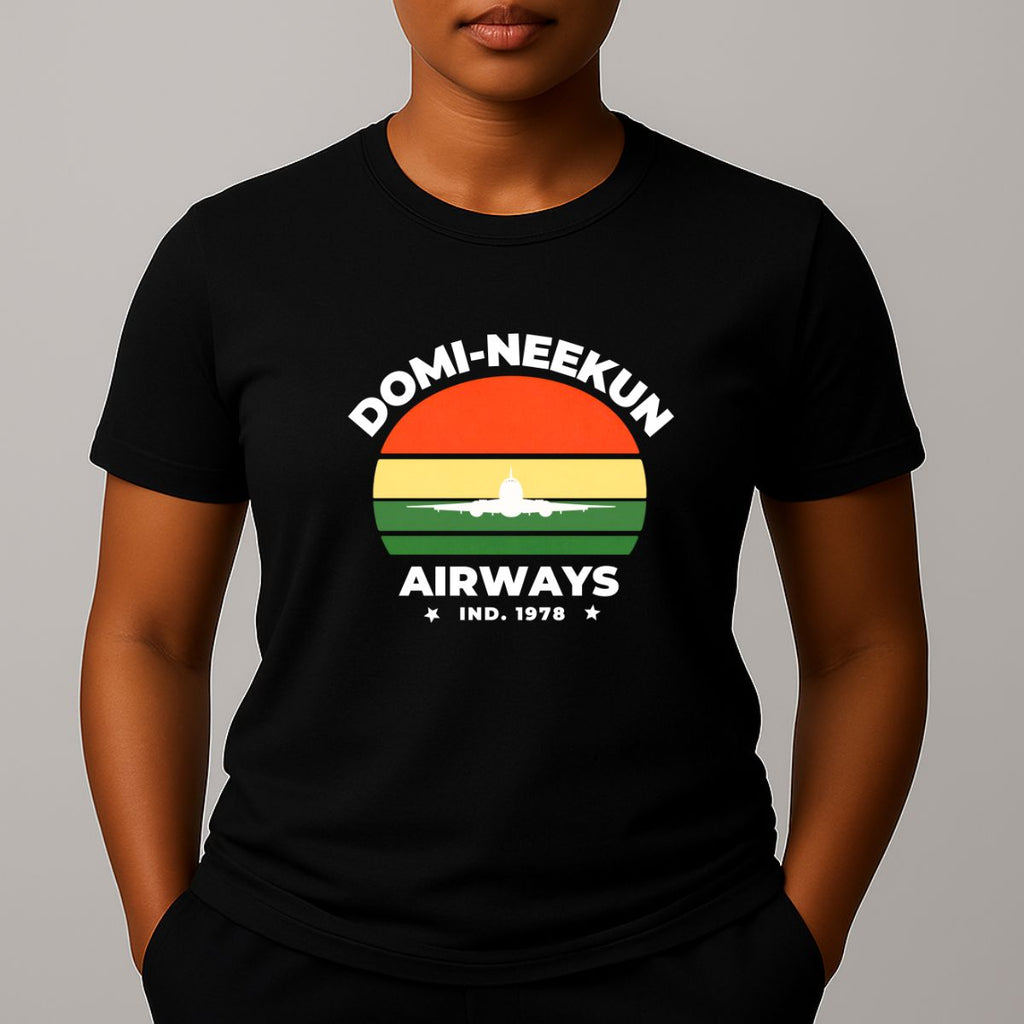 Person wearing a black short-sleeve T-shirt with a retro-style graphic reading 'DOMI-NEEKUN AIRWAYS' and 'IND. 1978' over a striped sunset and airplane silhouette.