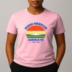 Person wearing a pink short-sleeve T-shirt with a retro-style graphic reading 'DOMI-NEEKUN AIRWAYS' and 'IND. 1978' over a striped sunset and airplane silhouette.