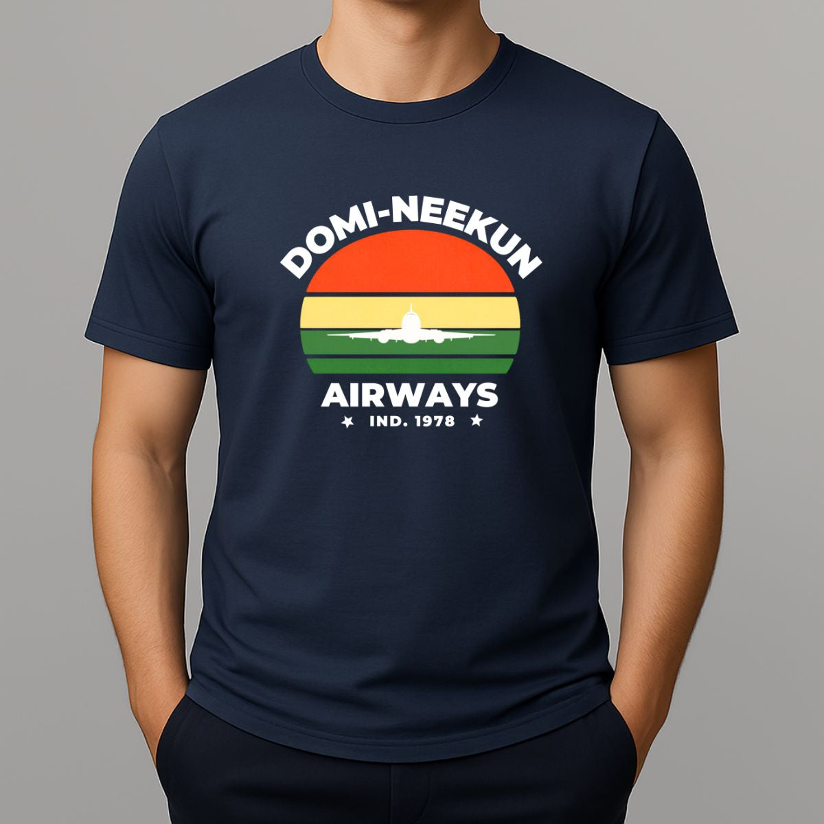 Person wearing a navy short-sleeve T-shirt with a retro-style graphic reading 'DOMI-NEEKUN AIRWAYS' and 'IND. 1978' over a striped sunset and airplane silhouette.