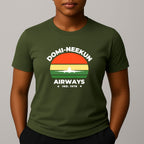 Person wearing a khaki green short-sleeve T-shirt with a retro-style graphic reading 'DOMI-NEEKUN AIRWAYS' and 'IND. 1978' over a striped sunset and airplane silhouette.