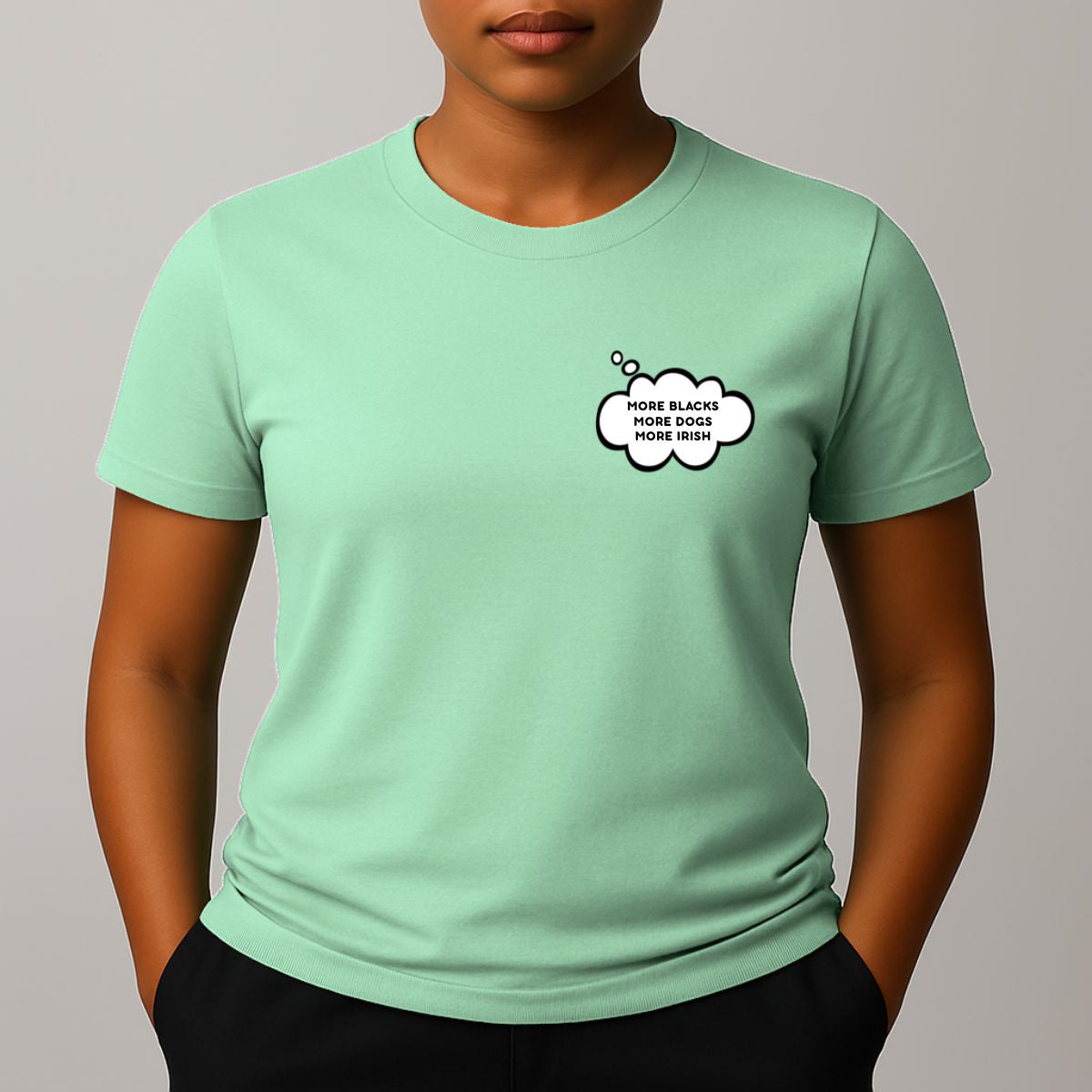 Person wearing a mint green short-sleeve t-shirt with a comic style thought bubble on the left chest. Black text reads "MORE BLACKS, MORE DOGS, MORE IRISH".