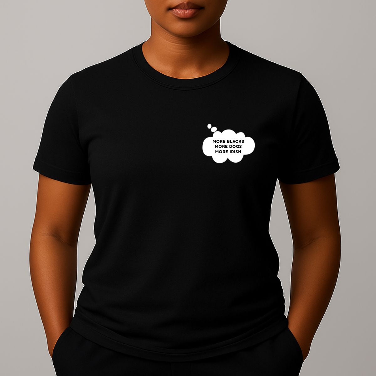Person wearing a black short-sleeve t-shirt with a comic style thought bubble on the left chest. Black text reads "MORE BLACKS, MORE DOGS, MORE IRISH".
