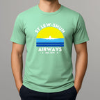 Person wearing an mint green t-shirt with a graphic print that reads 'ST LEW-SHUN AIRWAYS IND. 1979' in white, above and below a colourful striped circle with a white airplane in the center.