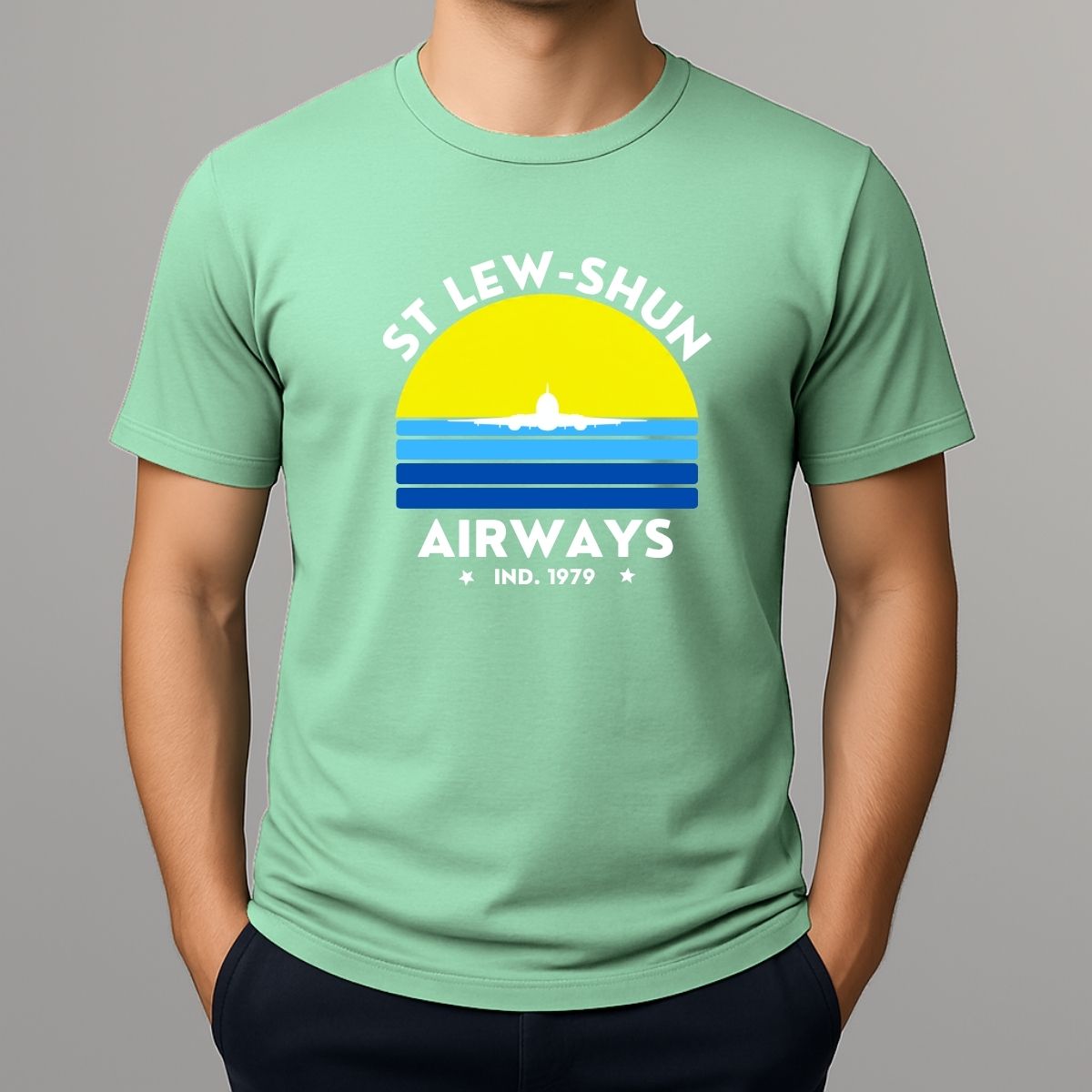 Person wearing an mint green t-shirt with a graphic print that reads 'ST LEW-SHUN AIRWAYS IND. 1979' in white, above and below a colourful striped circle with a white airplane in the center.