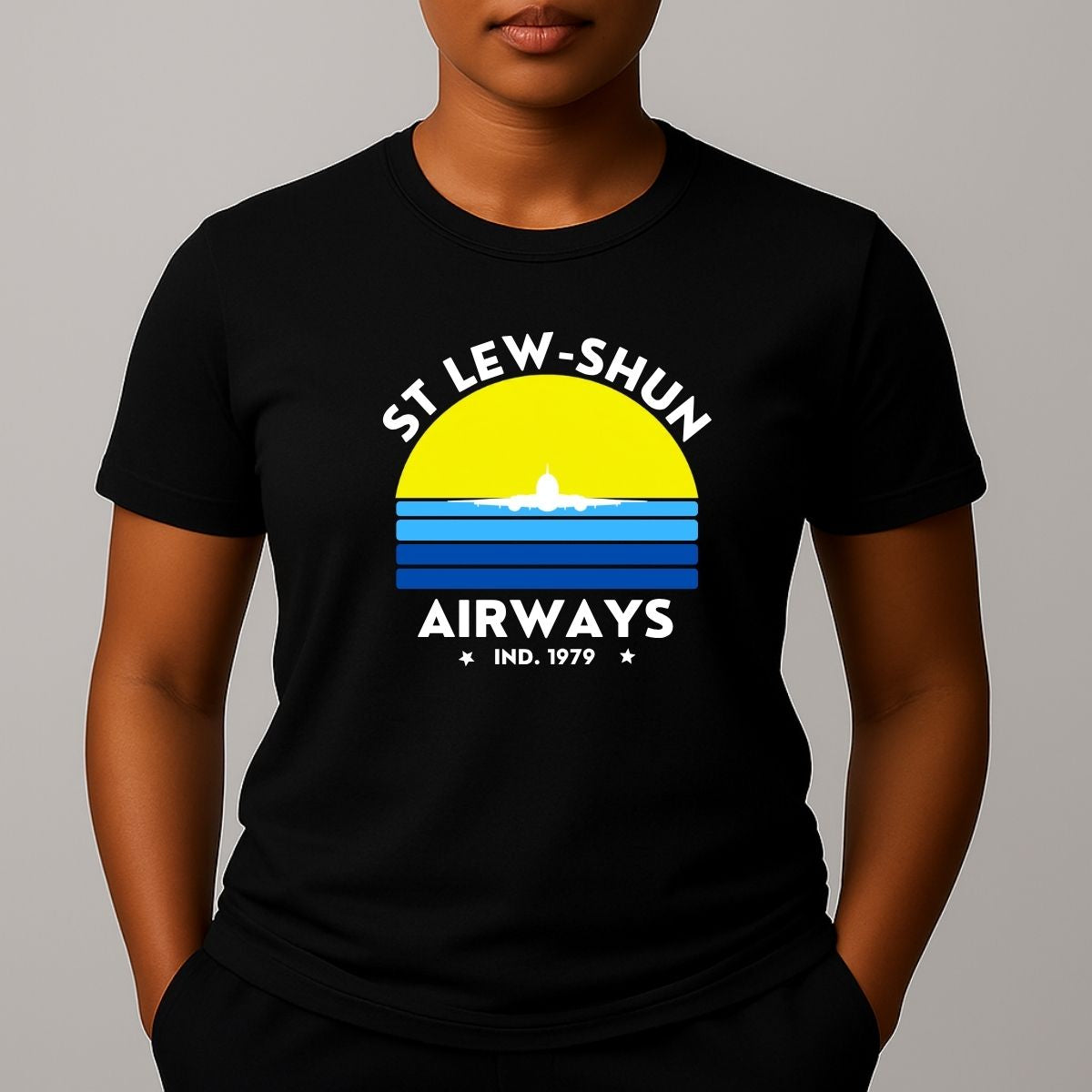 Person wearing an black t-shirt with a graphic print that reads 'ST LEW-SHUN AIRWAYS IND. 1979' in white, above and below a colourful striped circle with a white airplane in the center.