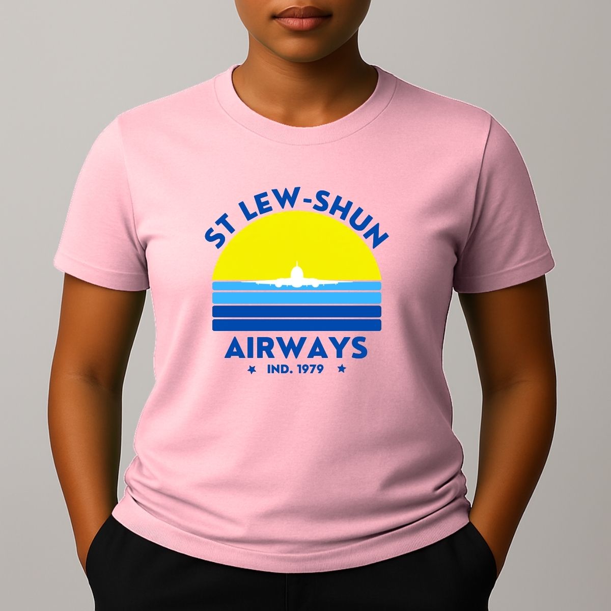 Person wearing an pink t-shirt with a graphic print that reads 'ST LEW-SHUN AIRWAYS IND. 1979' in blue, above and below a colourful striped circle with a white airplane in the center.