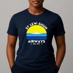 Person wearing an navy t-shirt with a graphic print that reads 'ST LEW-SHUN AIRWAYS IND. 1979' in white, above and below a colourful striped circle with a white airplane in the center.
