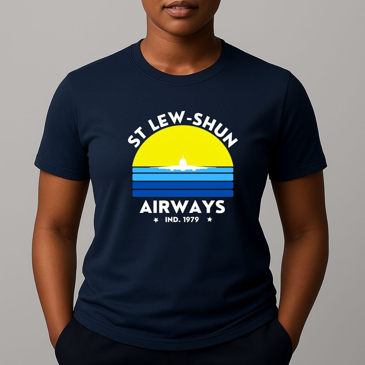 Person wearing an navy t-shirt with a graphic print that reads 'ST LEW-SHUN AIRWAYS IND. 1979' in white, above and below a colourful striped circle with a white airplane in the center.