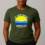 Person wearing an khaki green t-shirt with a graphic print that reads 'ST LEW-SHUN AIRWAYS IND. 1979' in white, above and below a colourful striped circle with a white airplane in the center.