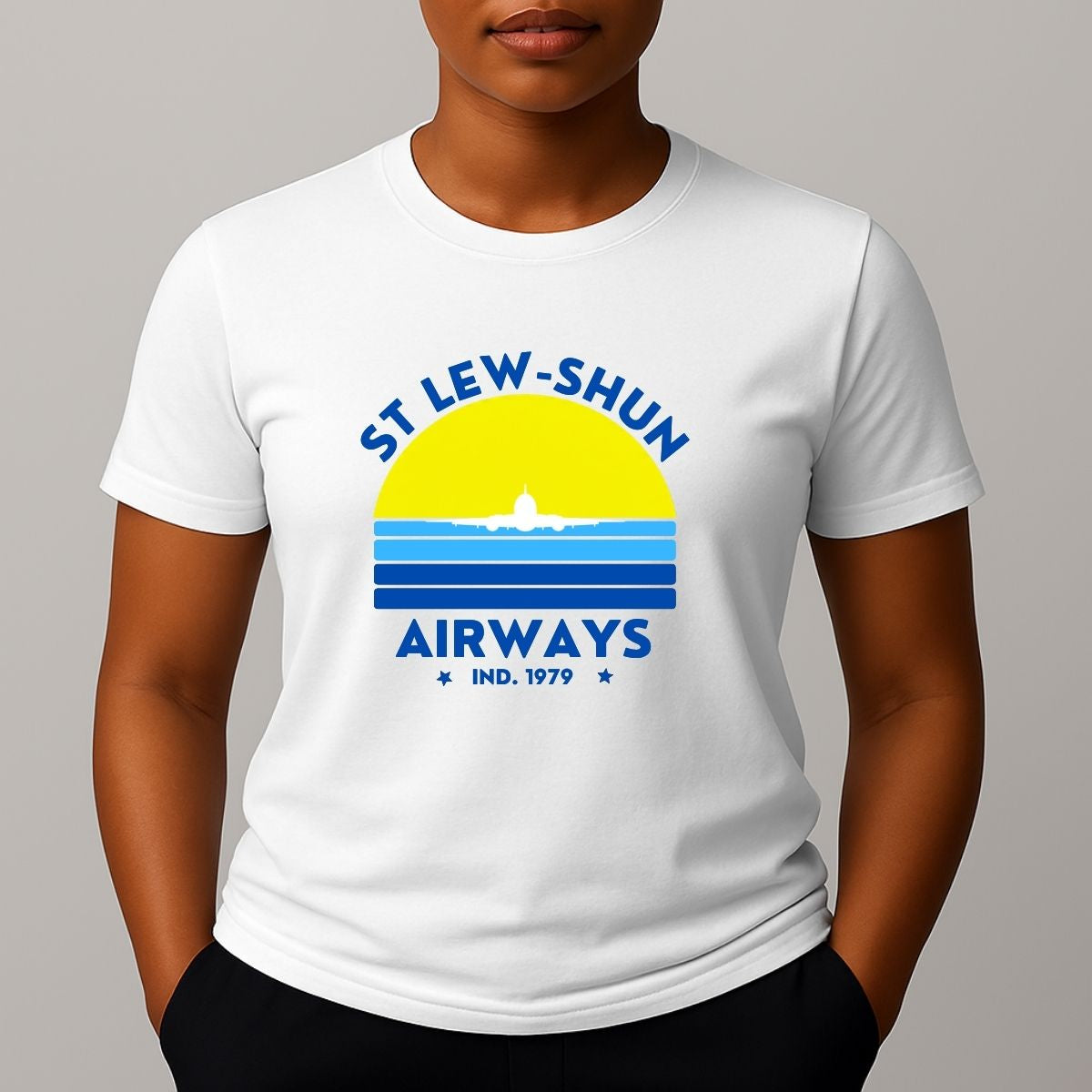 Person wearing an white t-shirt with a graphic print that reads 'ST LEW-SHUN AIRWAYS IND. 1979' in blue, above and below a colourful striped circle with a white airplane in the center.white