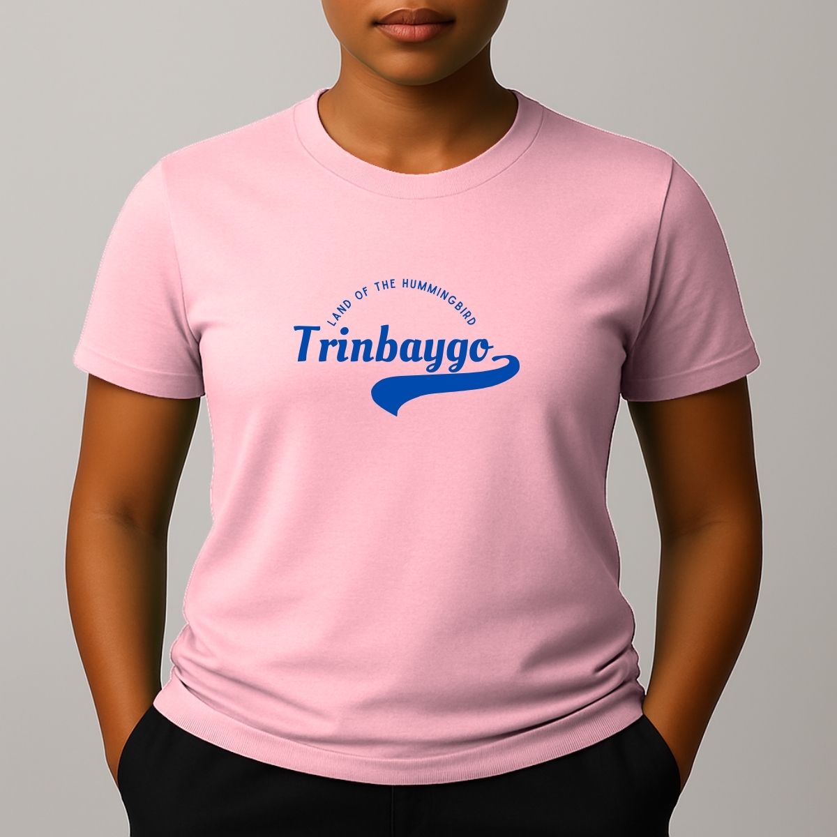Person wearing a pink t-shirt with a blue graphic print with a phonetic spelling that reads 'Trinbaygo' and 'LAND OF THE HUMMINGBIRD'.